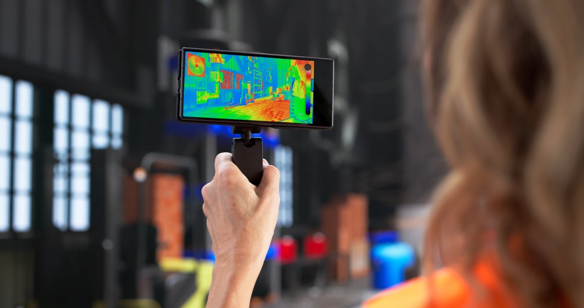 Female engineer using a thermal camera to inspect an HVAC system in a warehouse for moisture and leaks