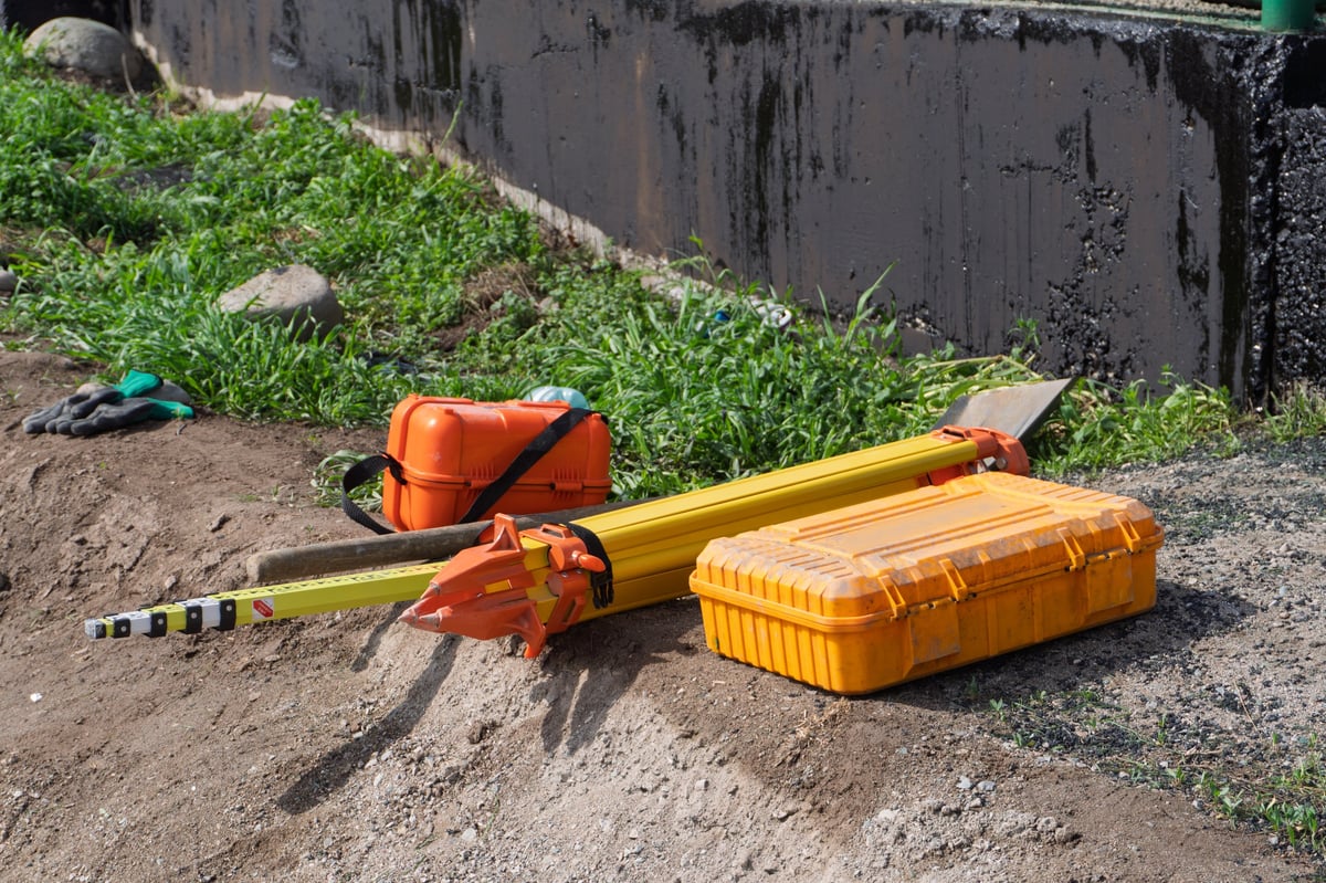 Professional surveying equipment including tripod, leveling staff, and protective cases used for underground pipe locating